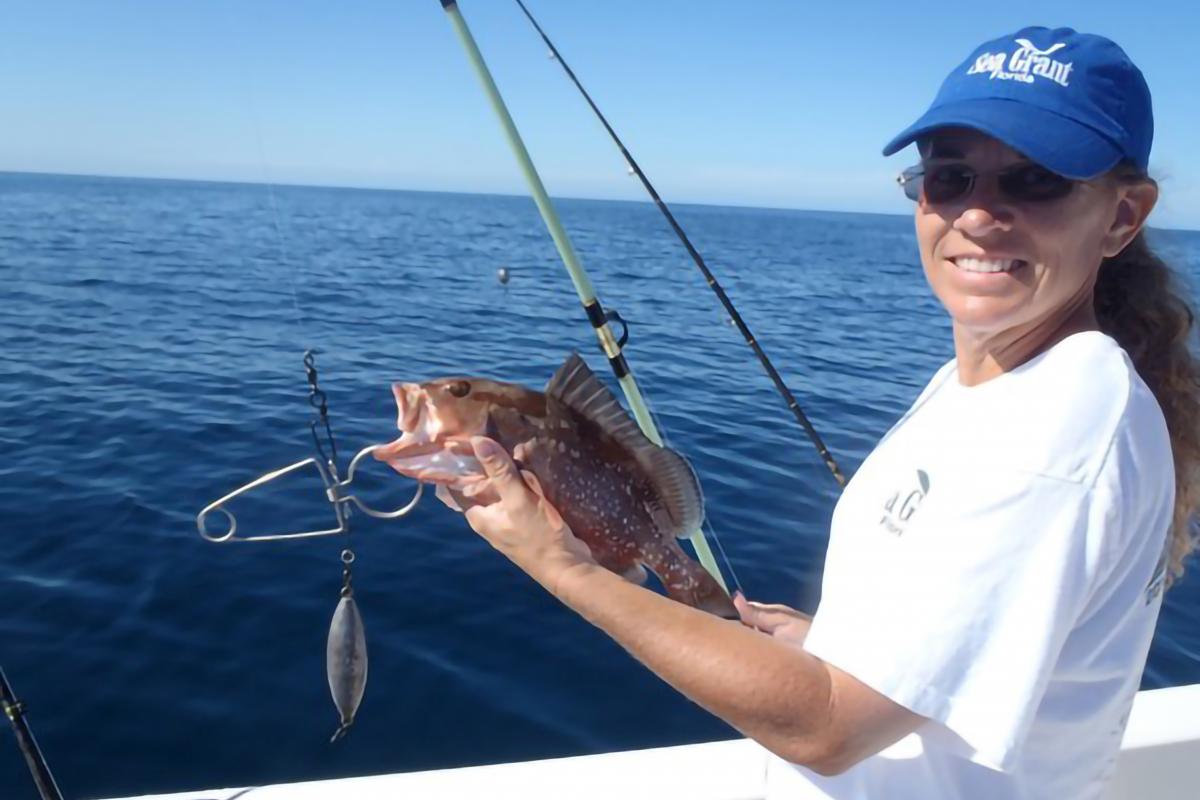 A person holding a fishing rod, fish, and barotrauma reduction device